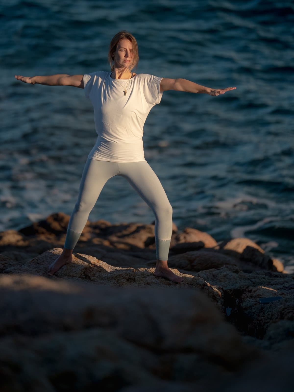 Jessy in Warrior II auf Felsen am Meer